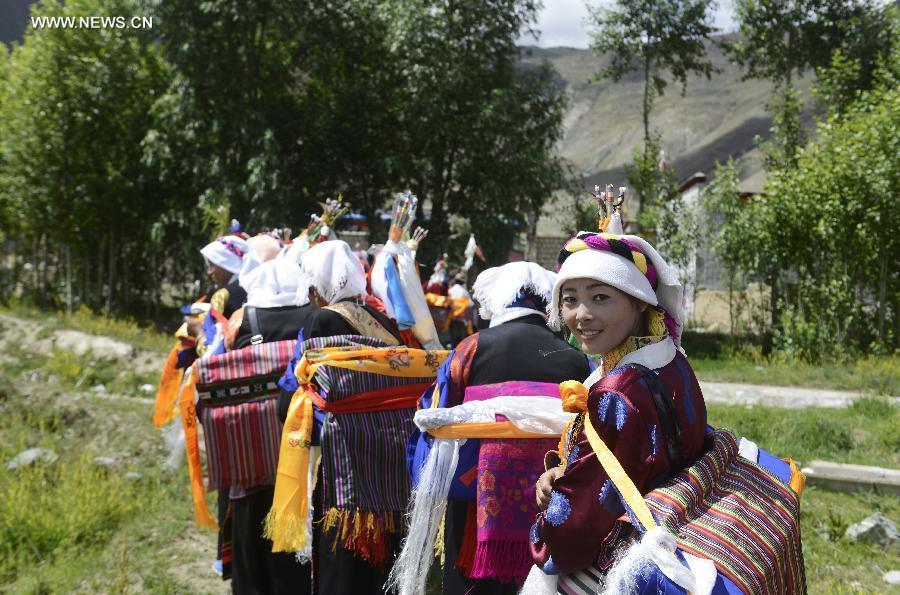 Farmers in holiday array carry scriptures while attending an Ongkor Festival prayer ceremony in Bomtoi Village, Dagze County, Lhasa, southwest China's Tibet Autonomous Region, July 1, 2014. By walking around farmlands, villagers of the Tibetan ethnic group pray for good harvests during the annual Ongkor Festival, or Bumper Harvest Festival. [Photo/Xinhua]