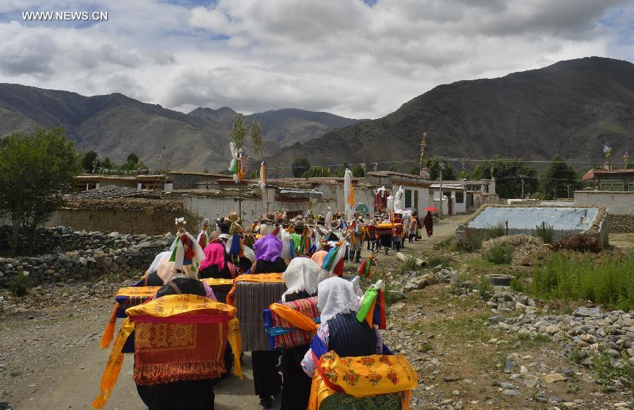 Farmers in holiday array carry scriptures while attending an Ongkor Festival prayer ceremony in Bomtoi Village, Dagze County, Lhasa, southwest China's Tibet Autonomous Region, July 1, 2014. By walking around farmlands, villagers of the Tibetan ethnic group pray for good harvests during the annual Ongkor Festival, or Bumper Harvest Festival. [Photo/Xinhua]