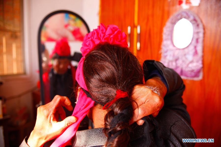 Flower Drum Dance performer Shi Chuncai puts on a flower on his head for performance in Lianhua Village, Huaiyuan County of Bengbu City, east China's Anhui Province, Dec 3, 2014. [Photo/Xinhua]